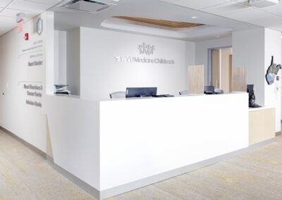 Image showcasing a white painted reception desk with silver wall-mounted ext and wooden desk separators within WVU Medicine Children's