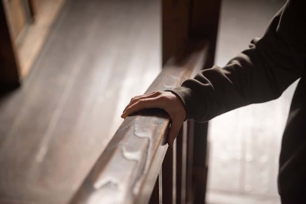 senior rests their hand on a smooth wooden handrail